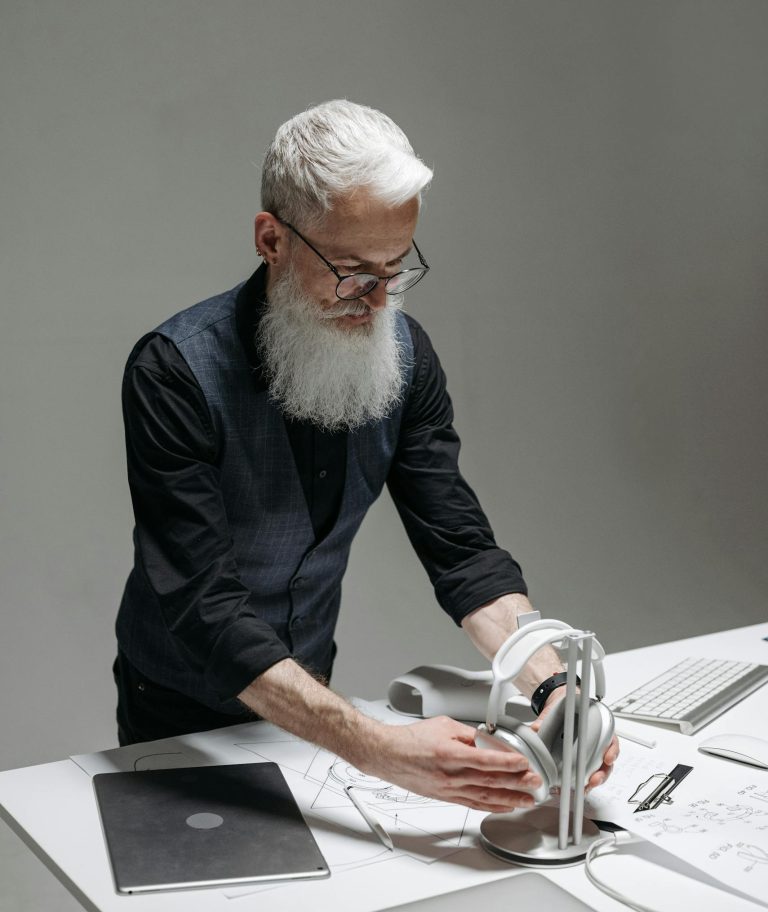 Elderly man with headphones working at a desk, using modern technology and gadgets.